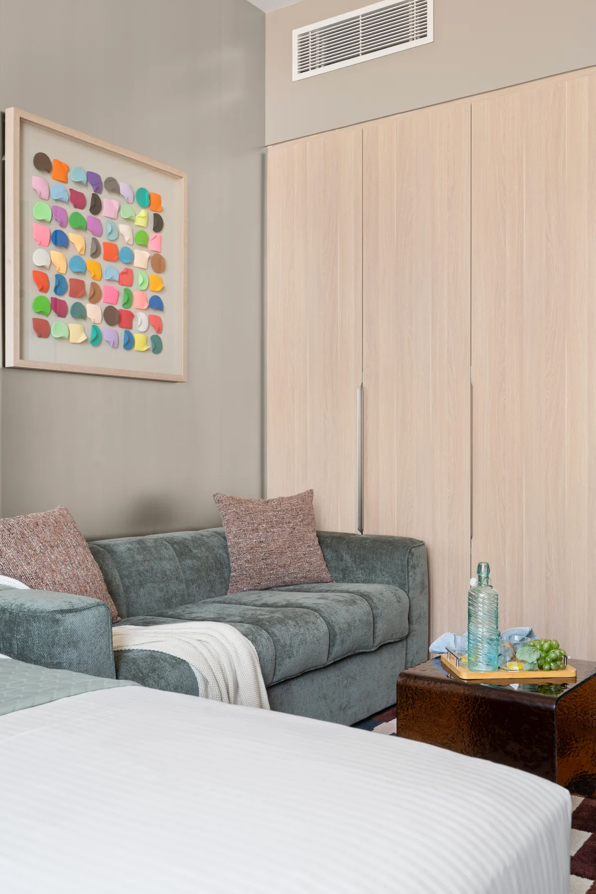 Un dormitorio con una zona de asientos gris, arte colorido enmarcado y una cama en primer plano.