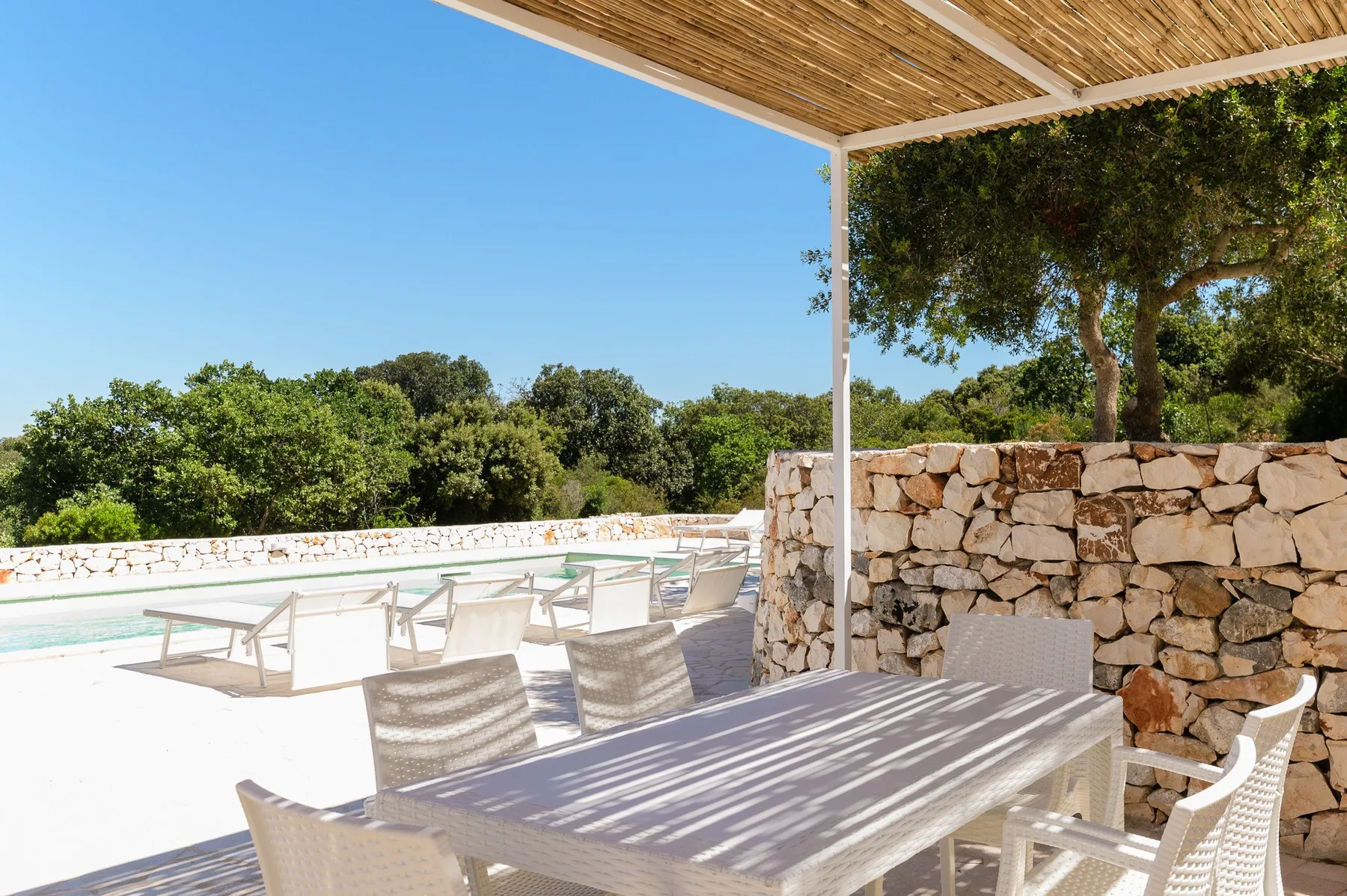 Un patio soleado con mesa de comedor, asientos y una piscina.