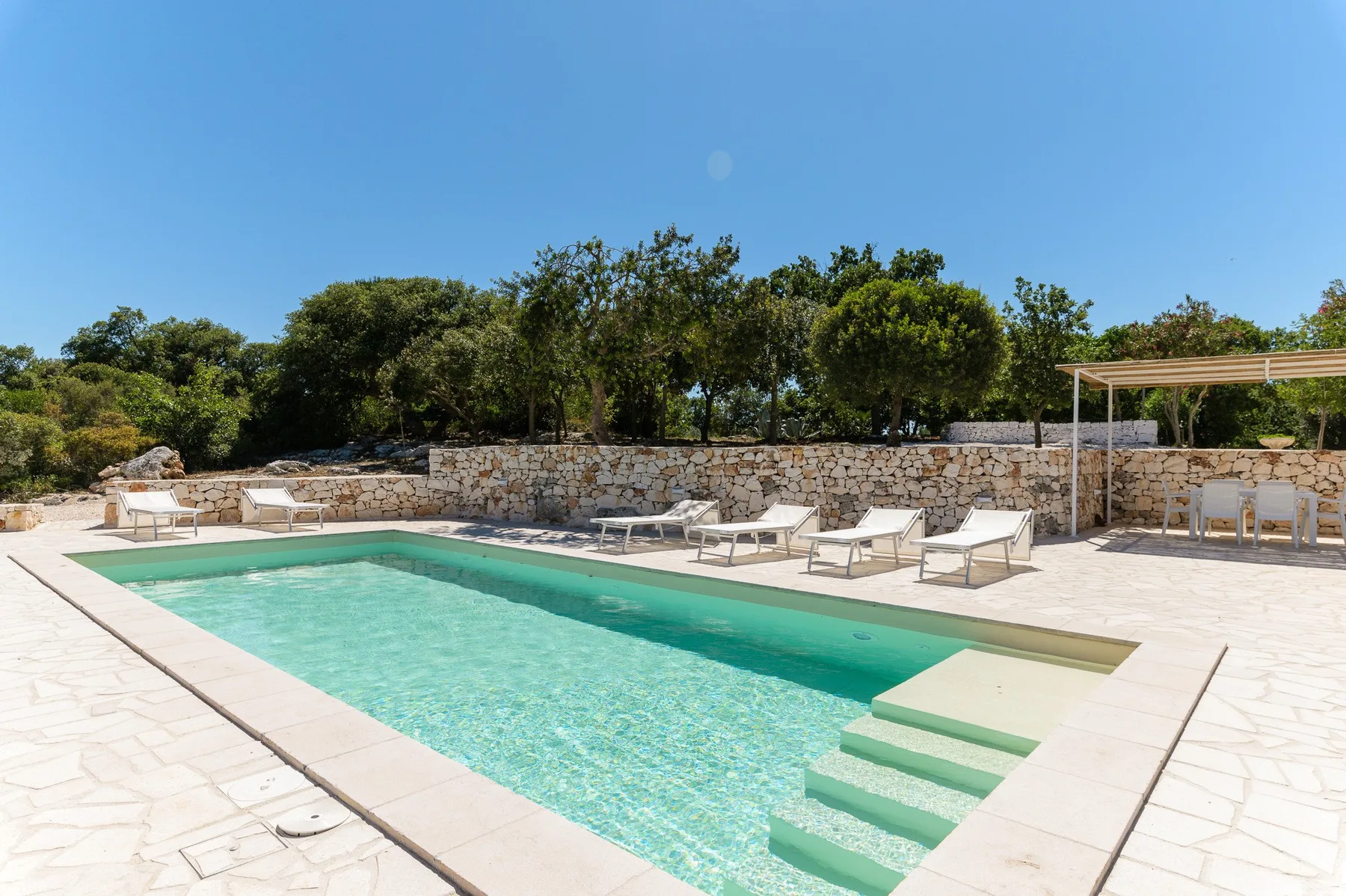 Piscina al aire libre con escalones poco profundos, rodeada por un muro de piedra y asientos.