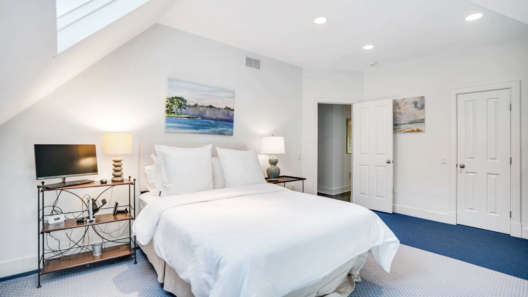 Un dormitorio luminoso con una cama blanca, mesitas de noche y techo inclinado.
