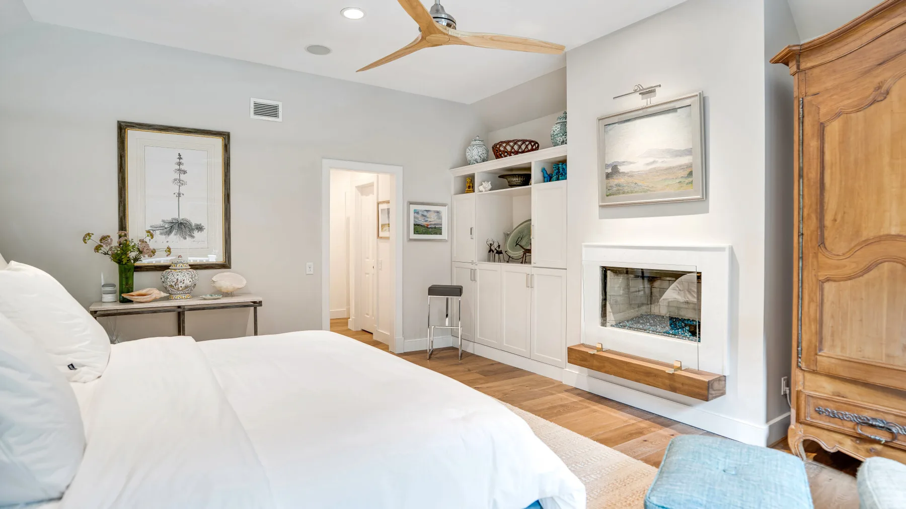 Un dormitorio con una cama blanca, estanterías empotradas y una chimenea.