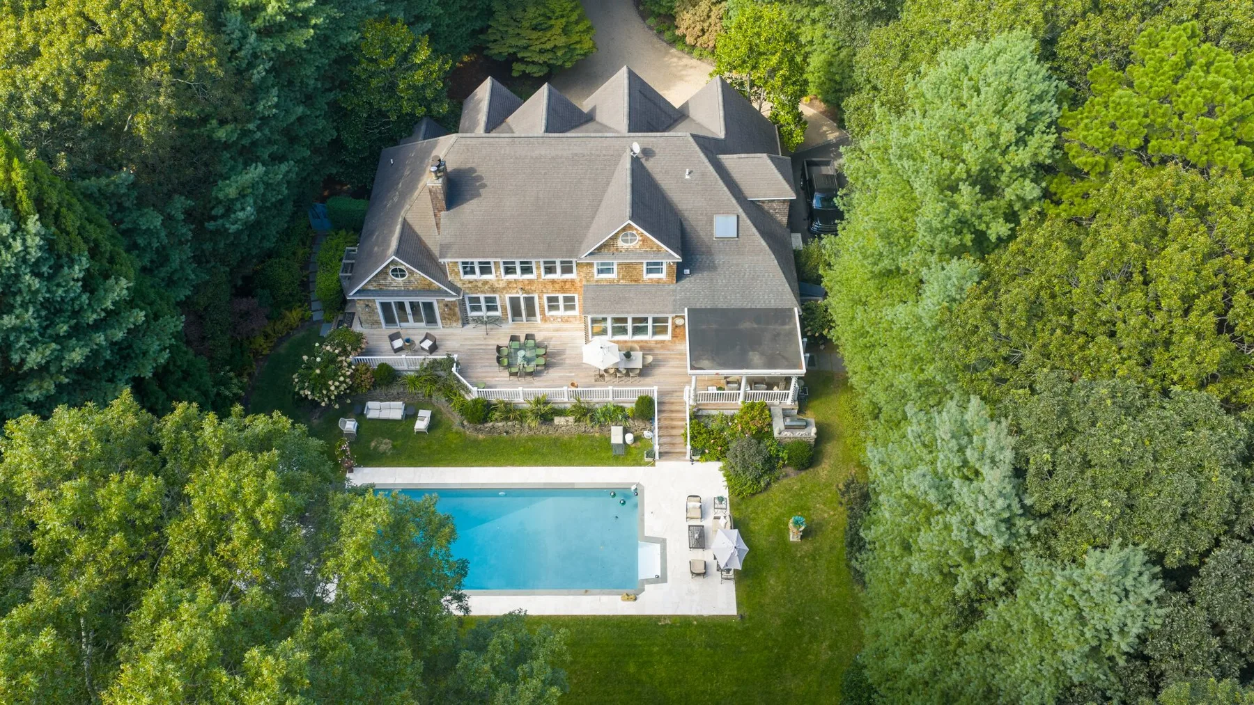 Vista aérea de una casa grande rodeada de árboles, con una piscina cerca.