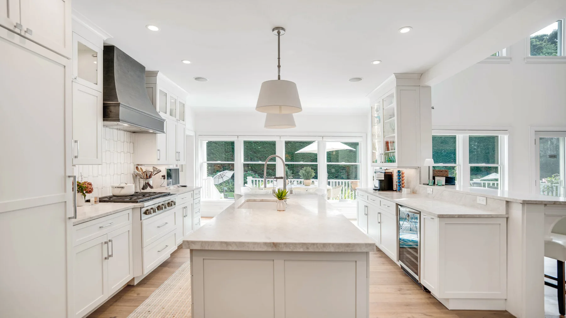 Una cocina blanca y luminosa con una isla central y ventanas con vistas a la vegetación.