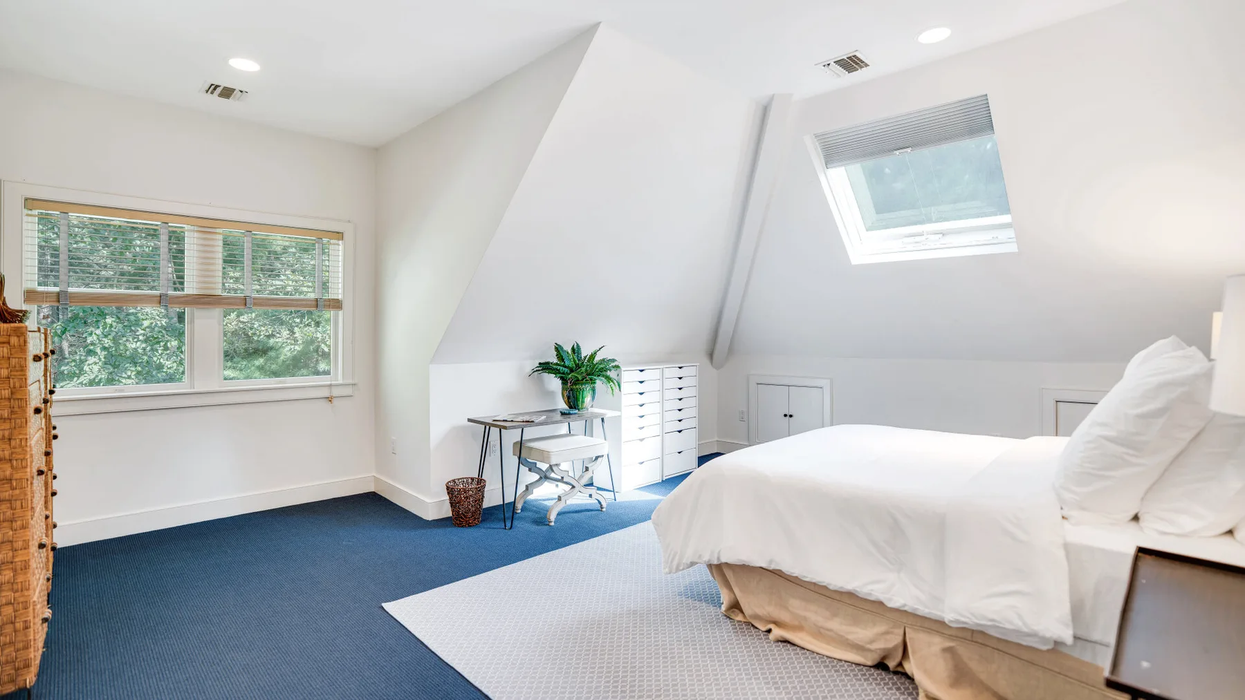 Un dormitorio luminoso tiene una cama, una ventana grande y un tragaluz.