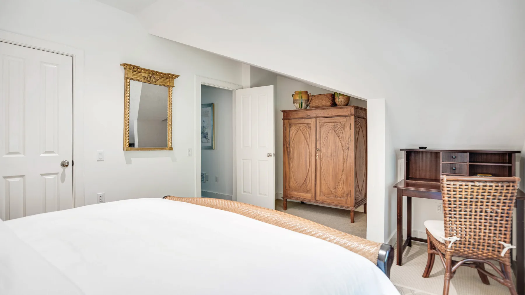 Un dormitorio luminoso con una cama grande, un armario de madera y un escritorio.