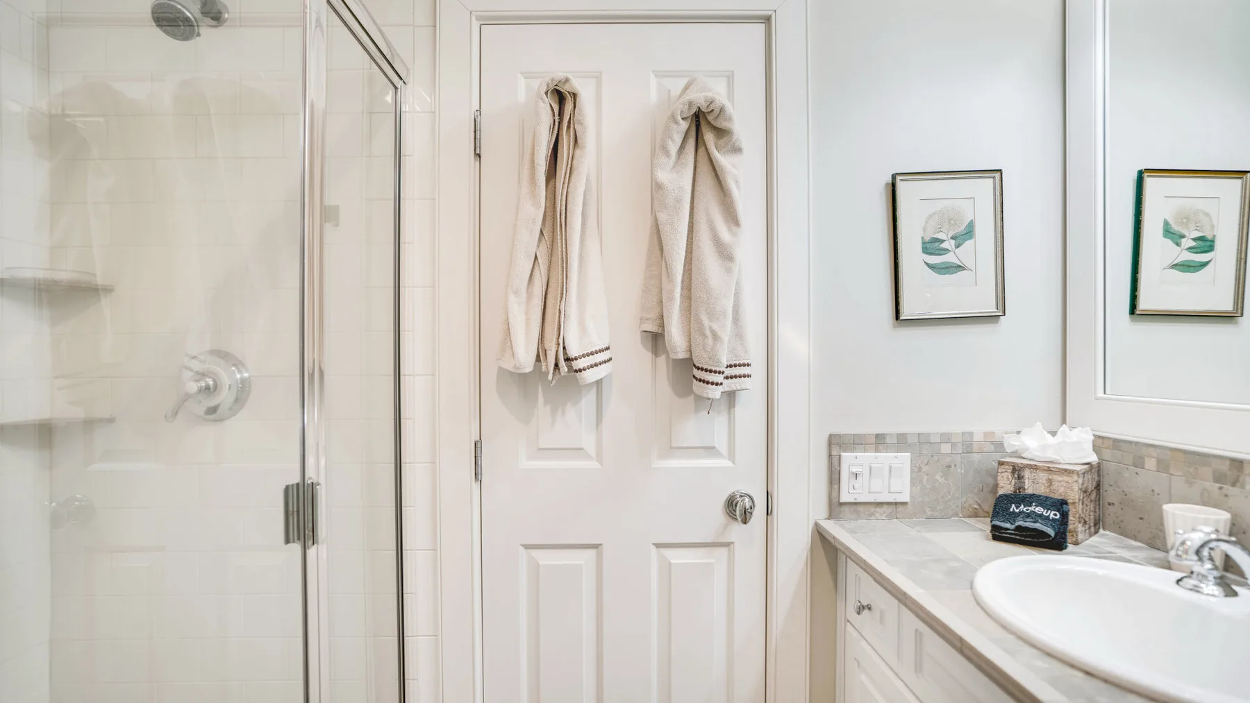 Un baño con ducha de vidrio, lavabo y toallas colgadas en la puerta.