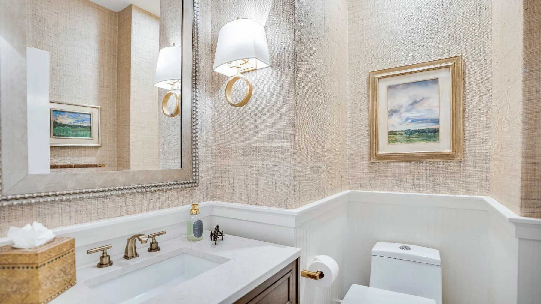 Un baño luminoso con un lavabo blanco y un cuadro de paisaje enmarcado.