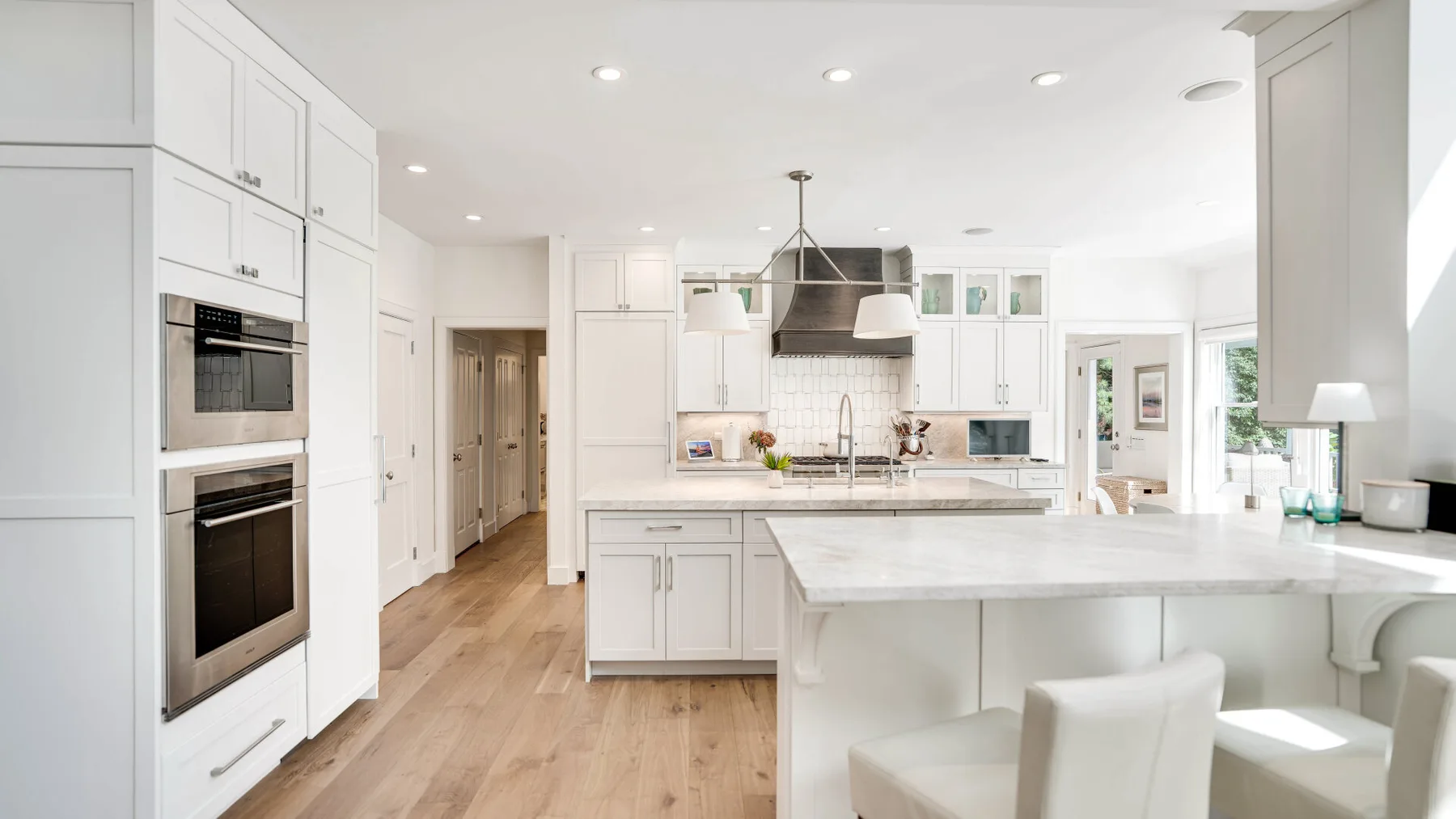 Una cocina luminosa con gabinetes blancos, una isla grande y piso de madera clara.