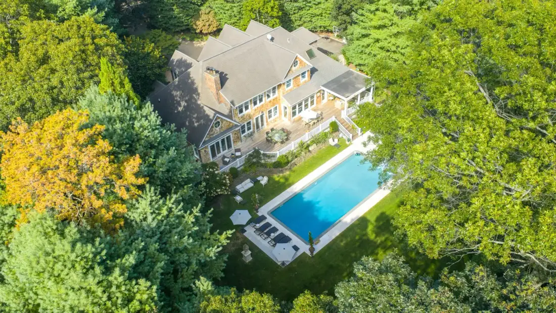 Vista aérea de una casa grande junto a una piscina rectangular, rodeada de árboles.