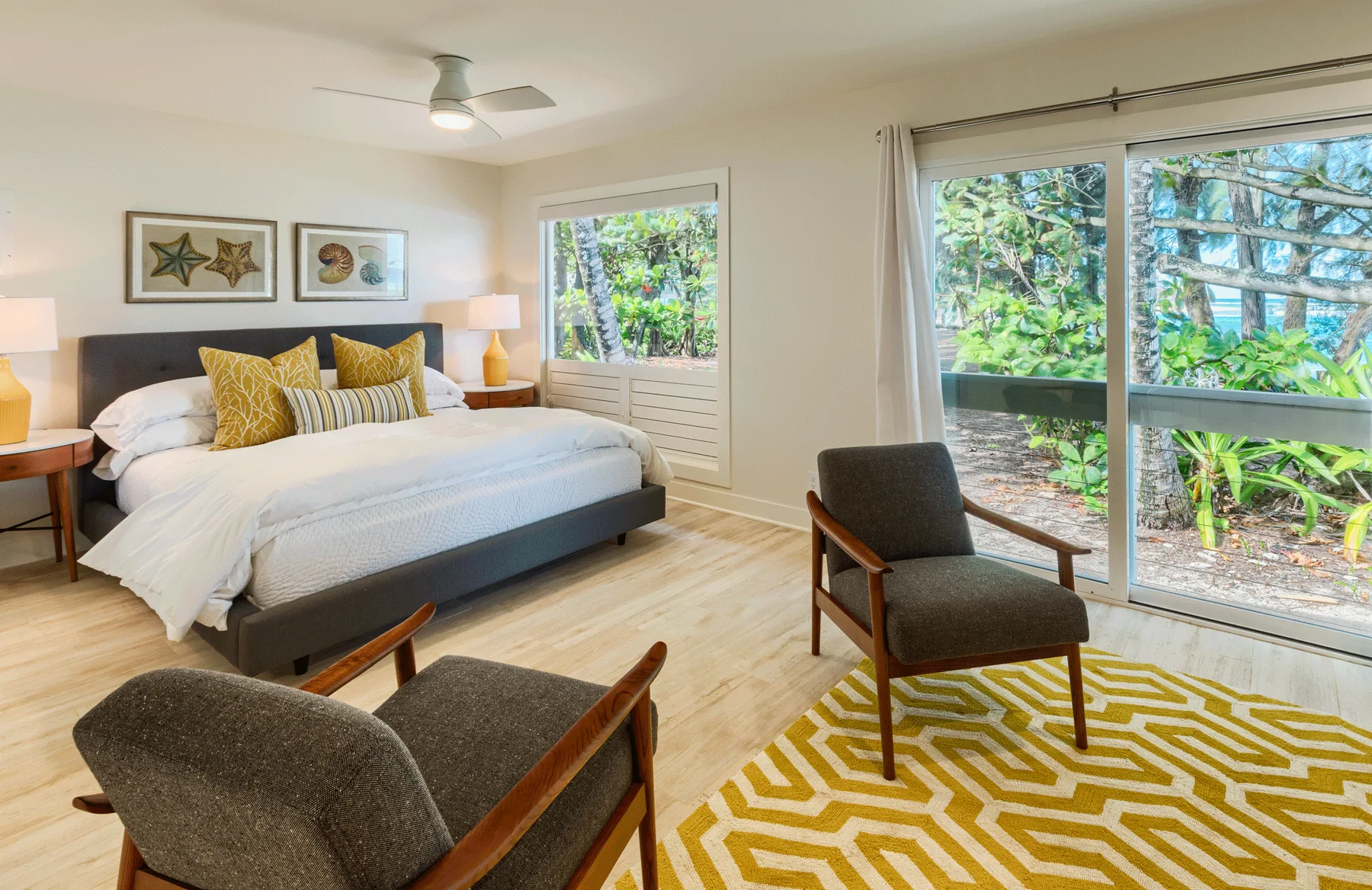 Un dormitorio con una cama, asientos y grandes ventanas con vistas a la vegetación.