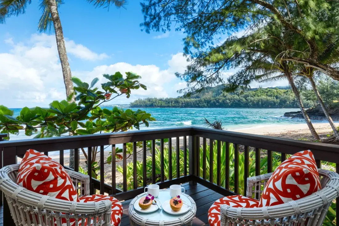 Una terraza con asientos acolchados da a una playa tropical y aguas turquesas.