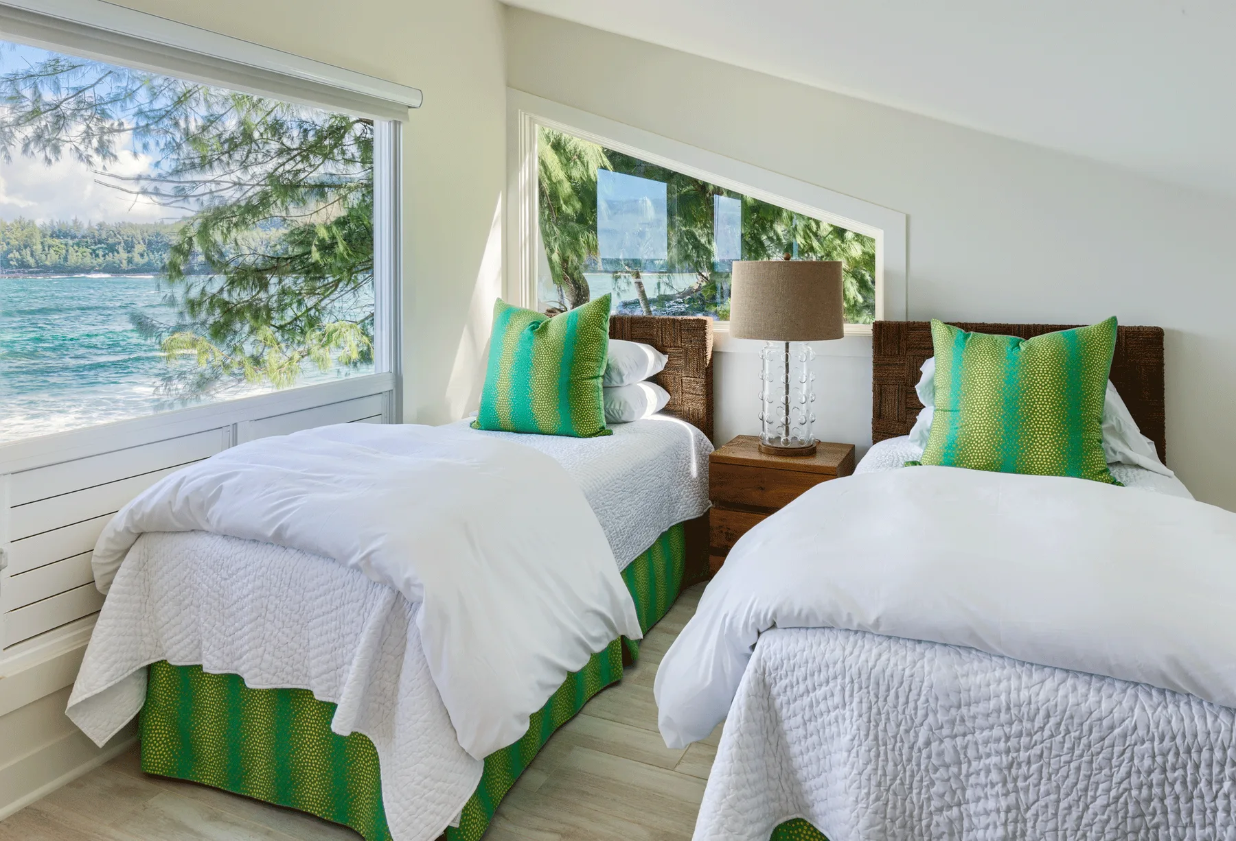 Un dormitorio luminoso con dos camas junto a una gran ventana con vistas al agua.