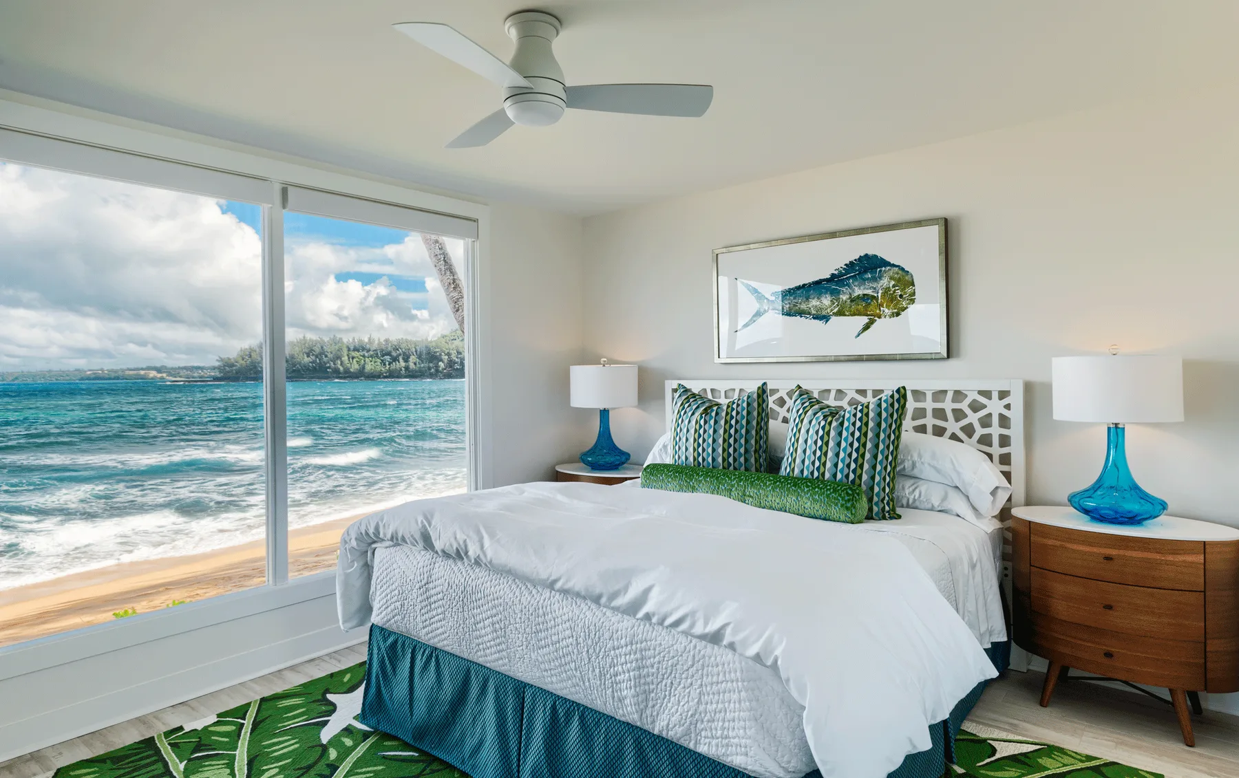 Un dormitorio luminoso con una cama junto a grandes ventanas con vistas al océano.