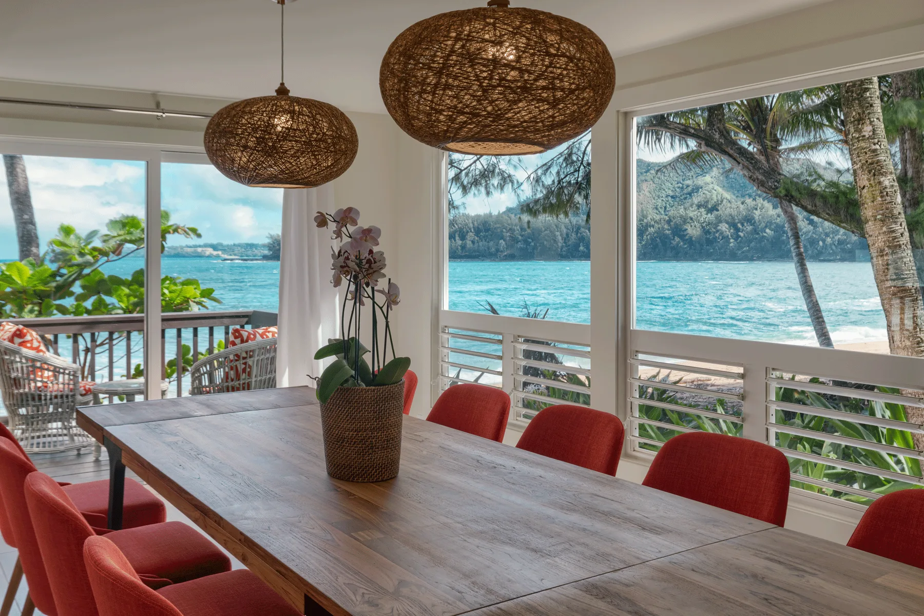 Un comedor con una mesa larga y asientos rojos tiene vistas al agua.