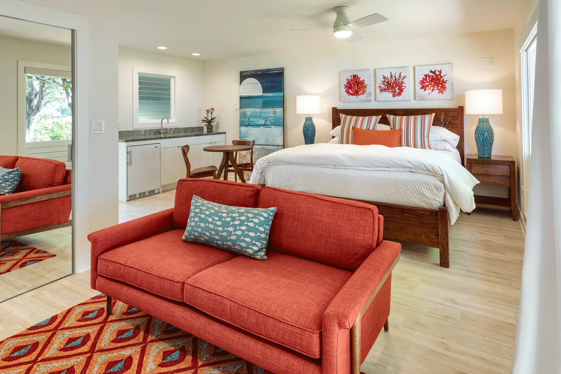 Un dormitorio luminoso con cama, asientos rojos y una pequeña cocina.