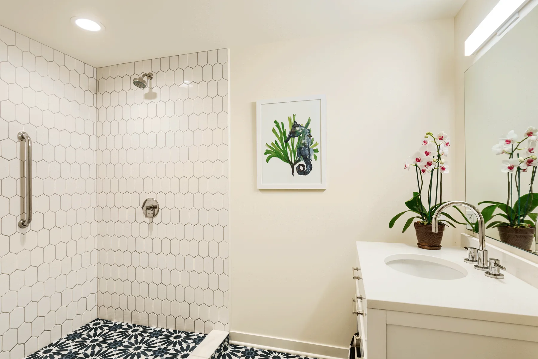 Un baño luminoso con ducha de azulejos, lavabo y orquídea en maceta.