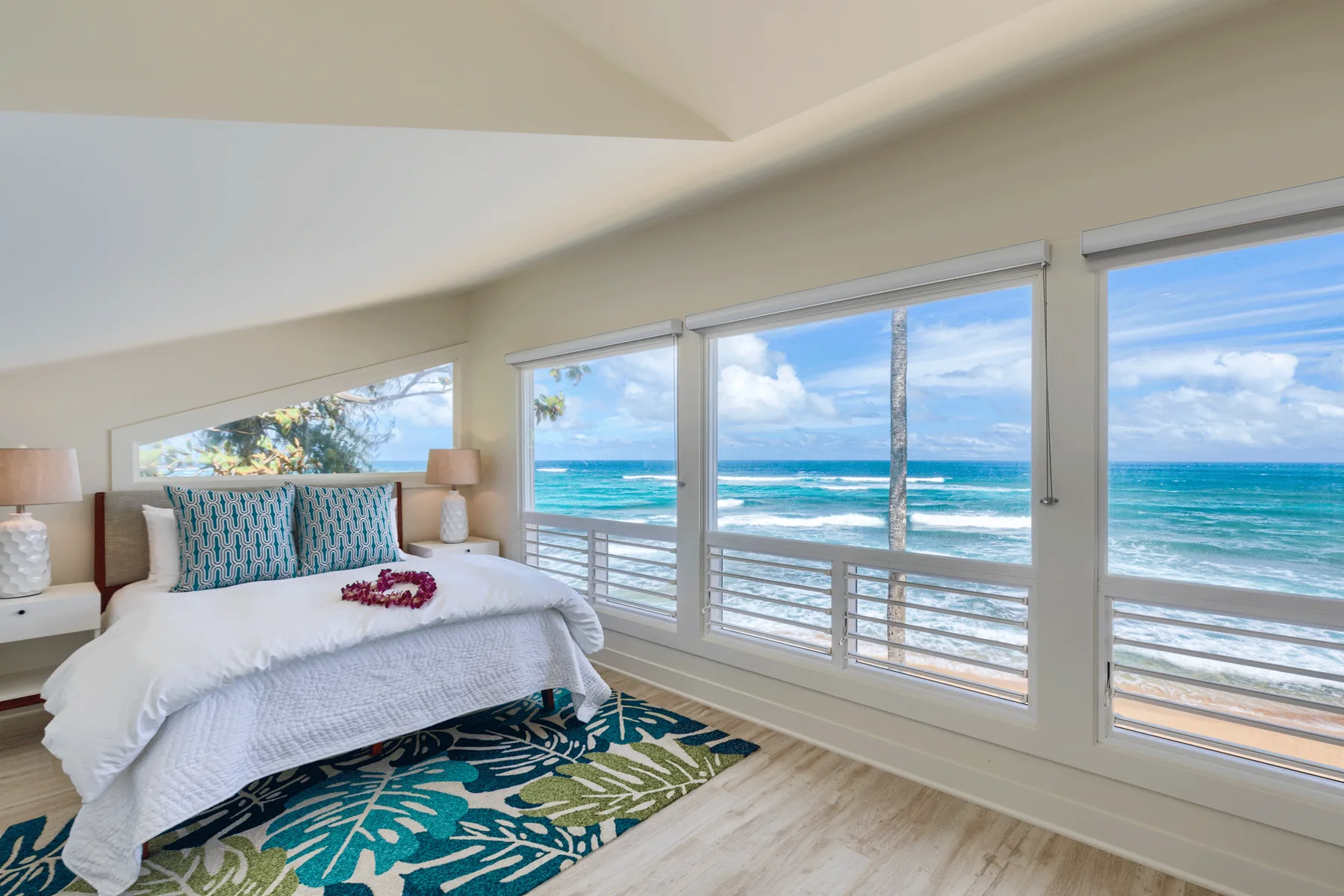 Un dormitorio luminoso con una cama junto a grandes ventanas con vistas al océano.