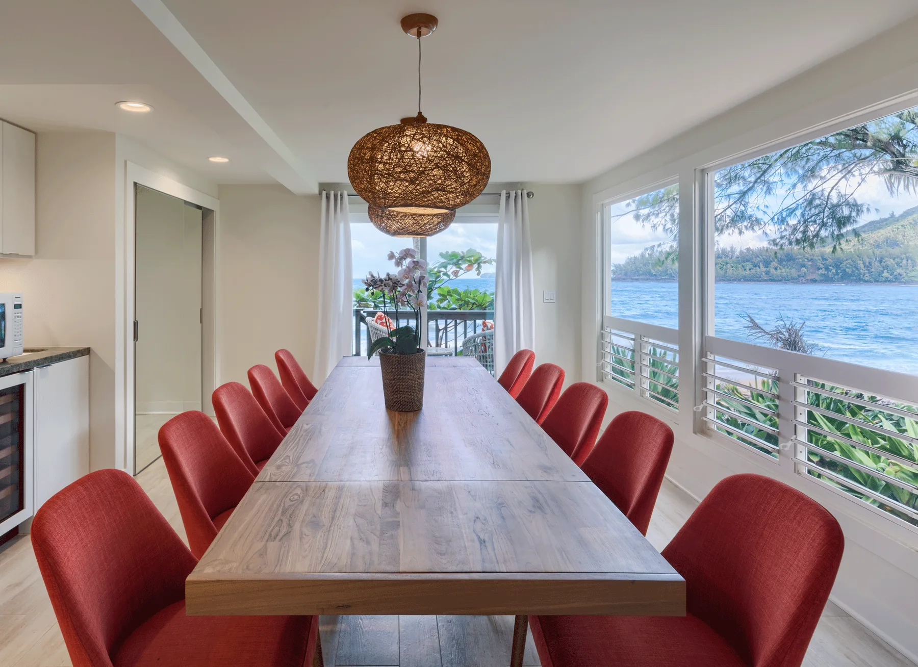 Comedor con una mesa larga y asientos rojos junto a grandes ventanas con vistas al agua.