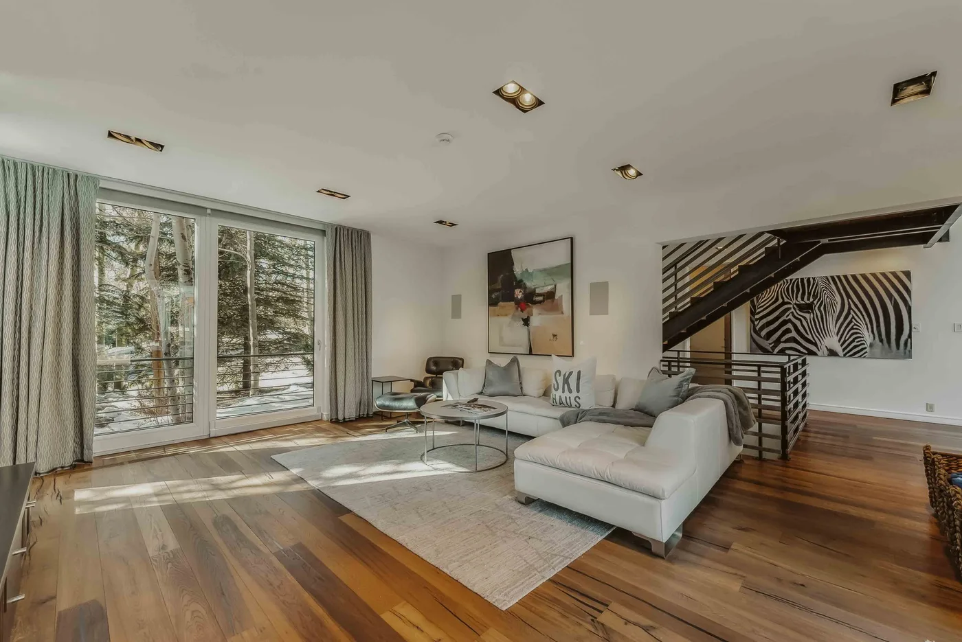 A bright living room with seating, large windows, and a staircase.