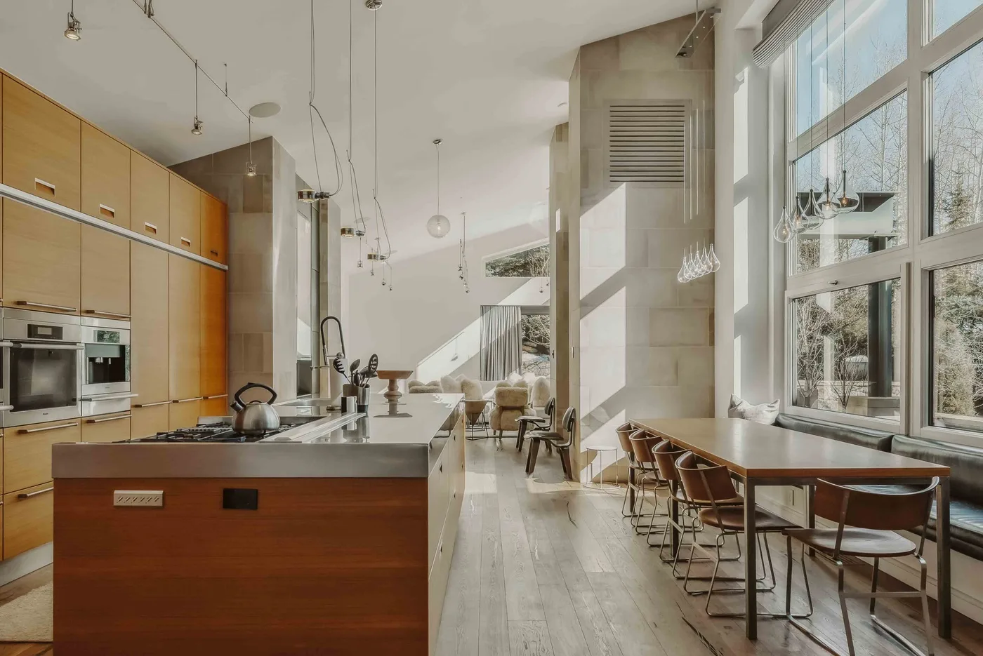 A bright open kitchen and dining area with a long table beside large windows.