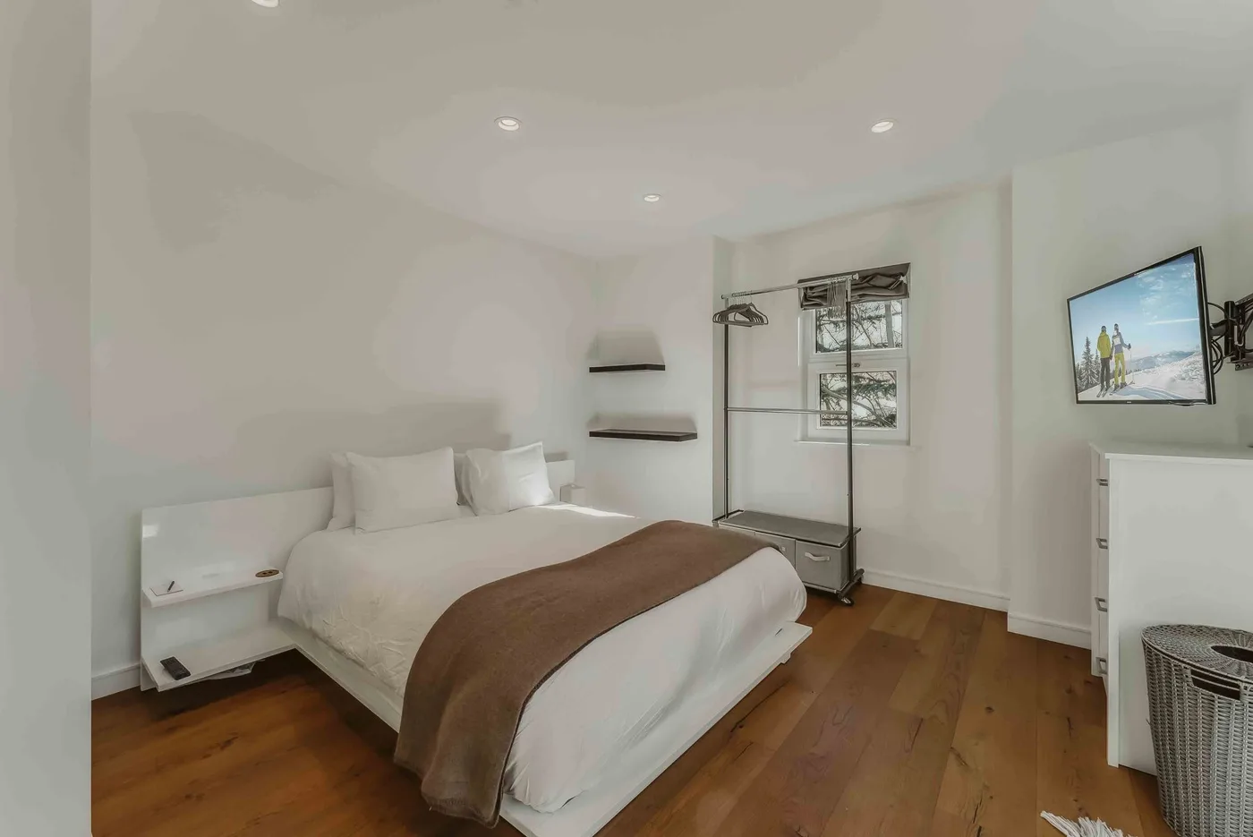 A bright bedroom with a bed, wooden flooring, and a window.