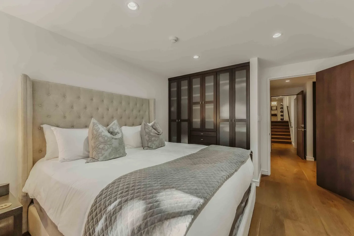A bedroom with a large bed, patterned cushions, and dark glass-paneled doors.