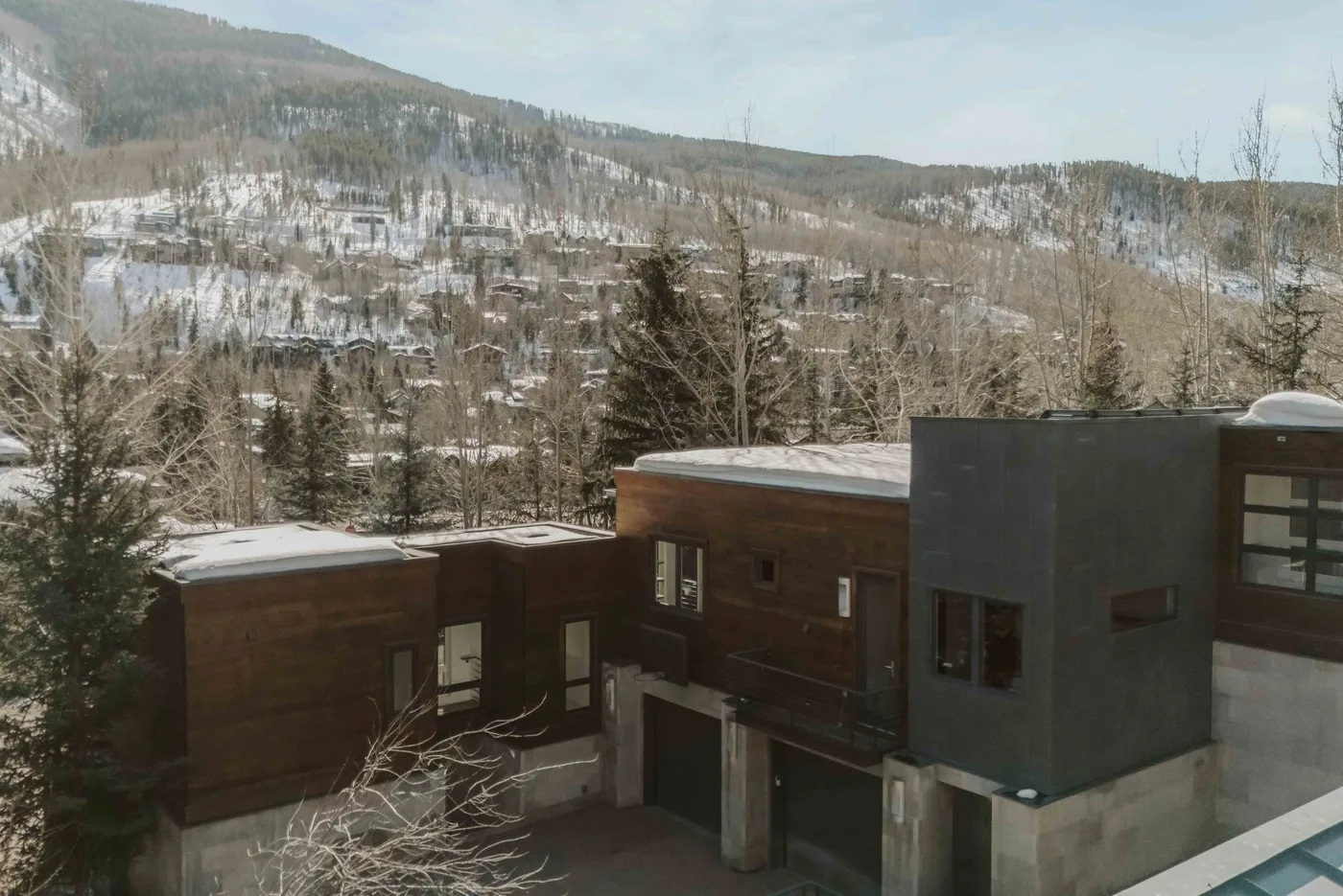 A modern building stands among snow-dusted trees with a mountain slope in the background.