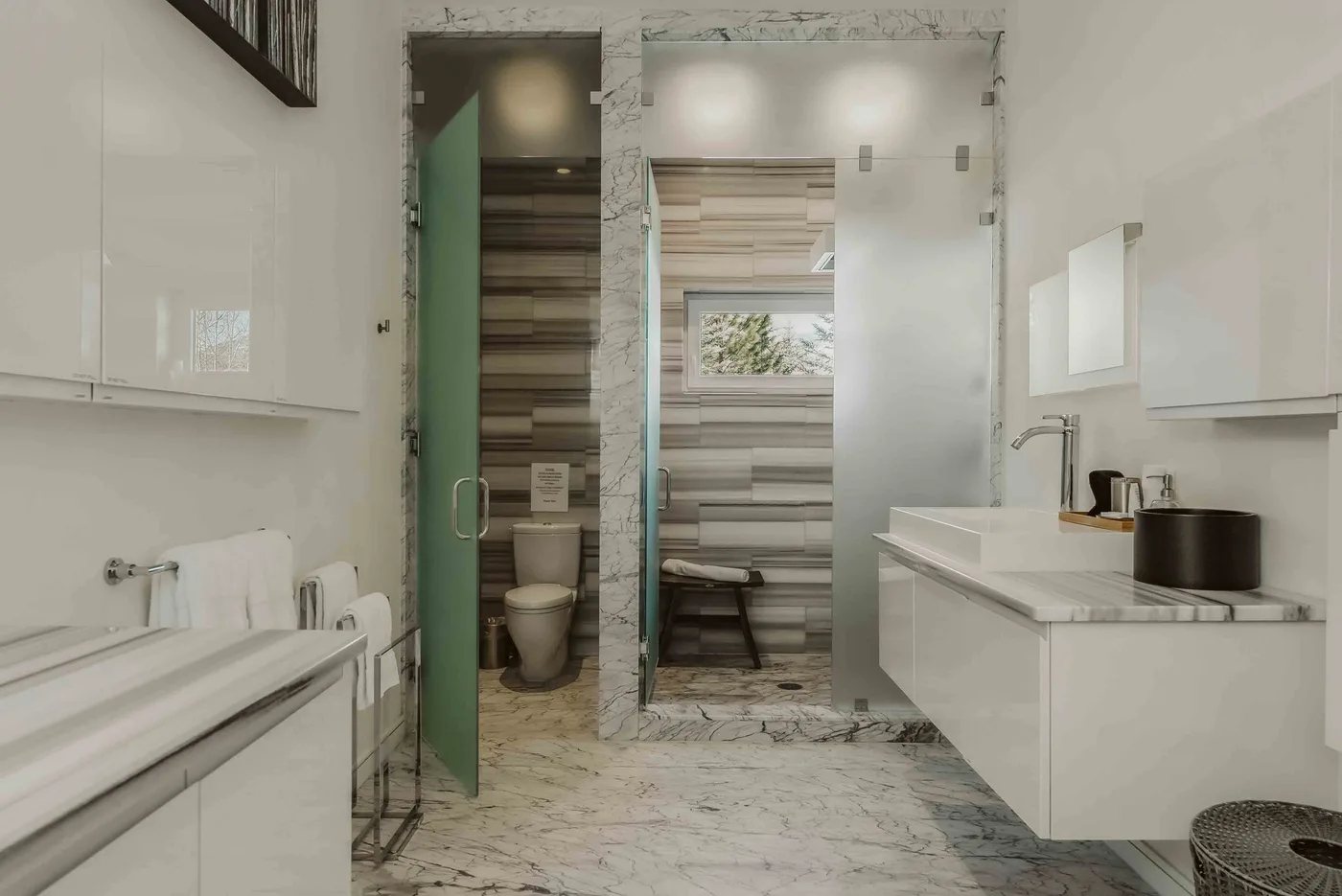 A modern bathroom with a glass shower, white vanity, and marble-patterned surfaces.
