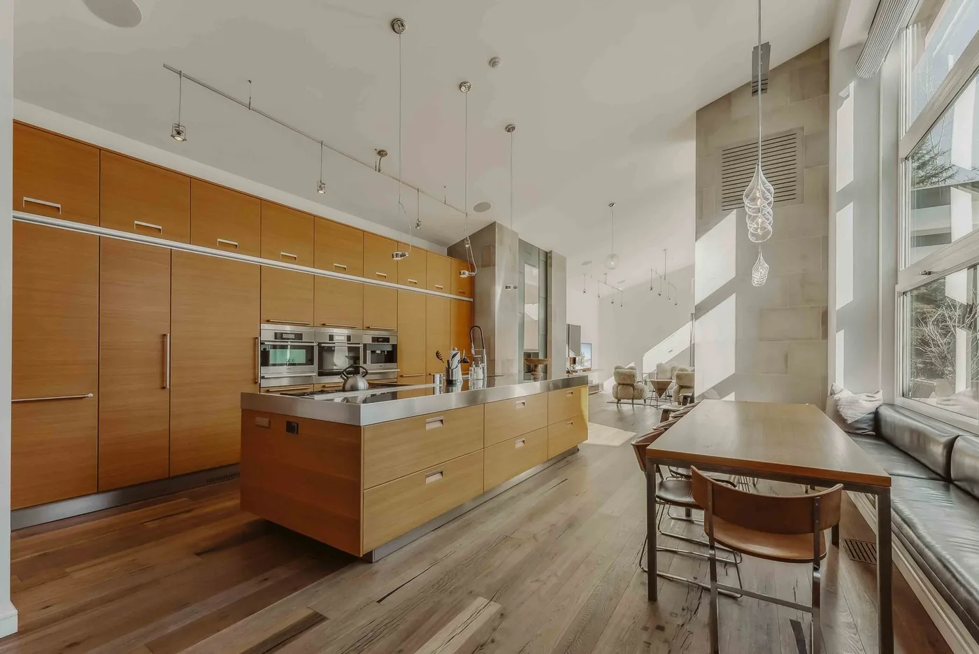 A bright open-plan kitchen and dining area with wooden cabinetry and a long table.