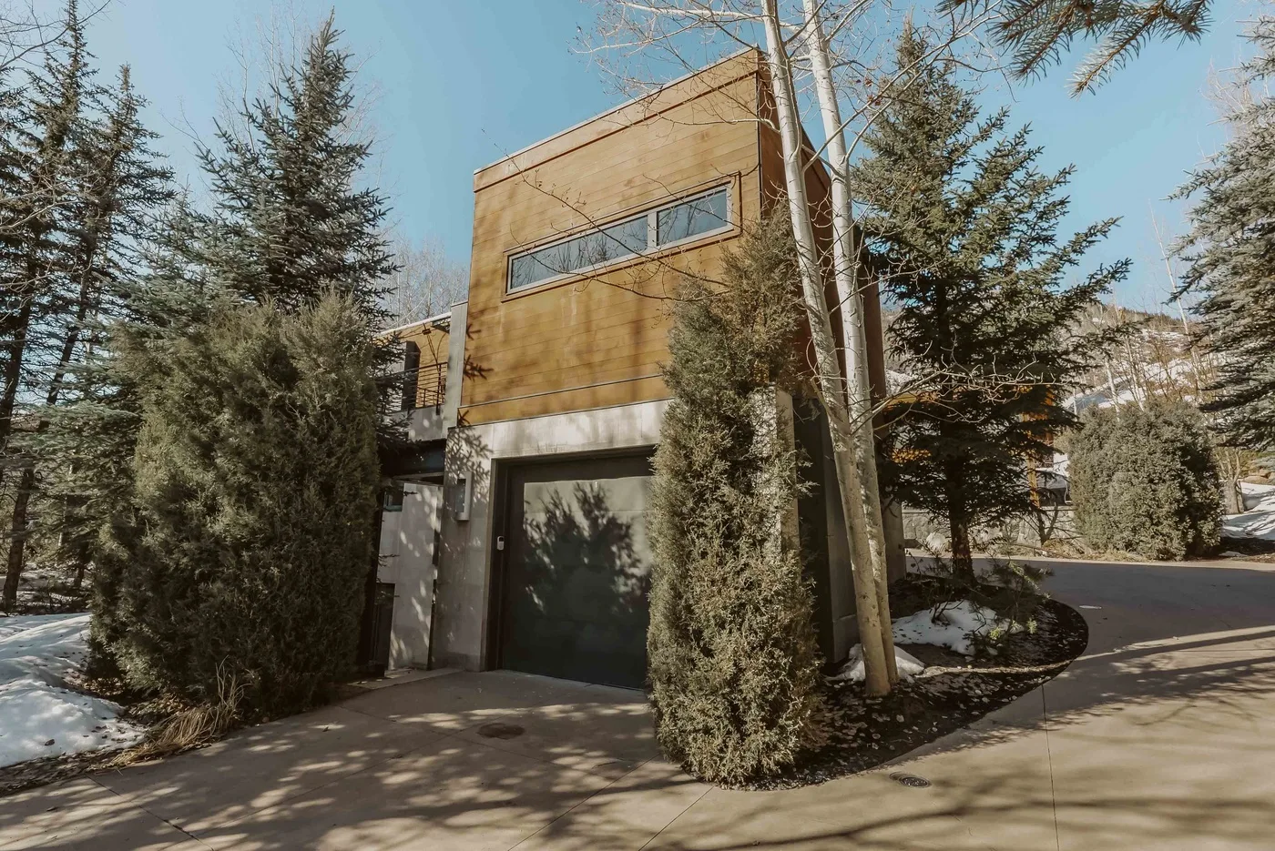 A modern house exterior with a garage entrance, trees, and a paved driveway.