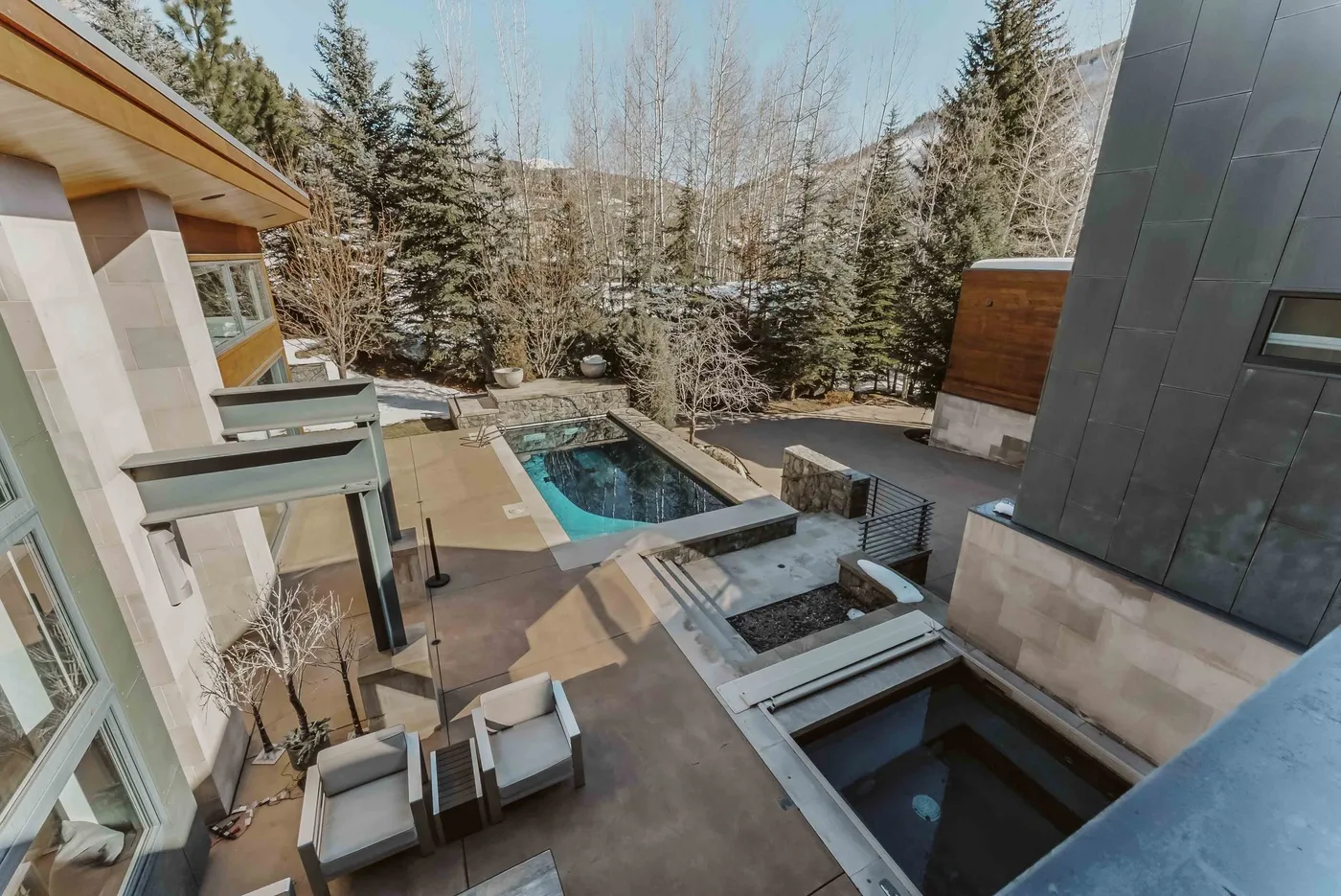 An outdoor patio with a swimming pool and seating, surrounded by trees.
