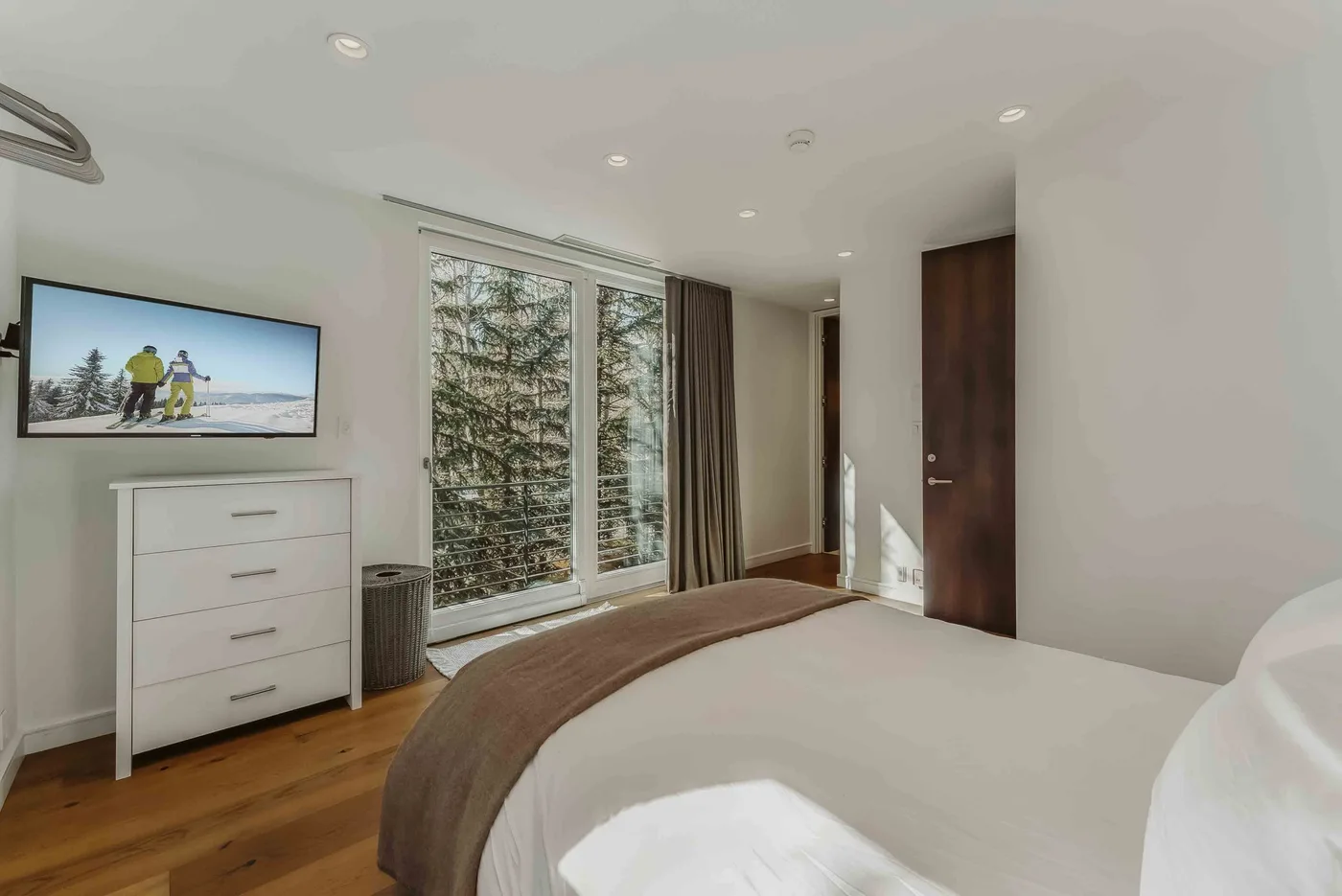 A bedroom with a bed, dresser, and large windows overlooking trees.