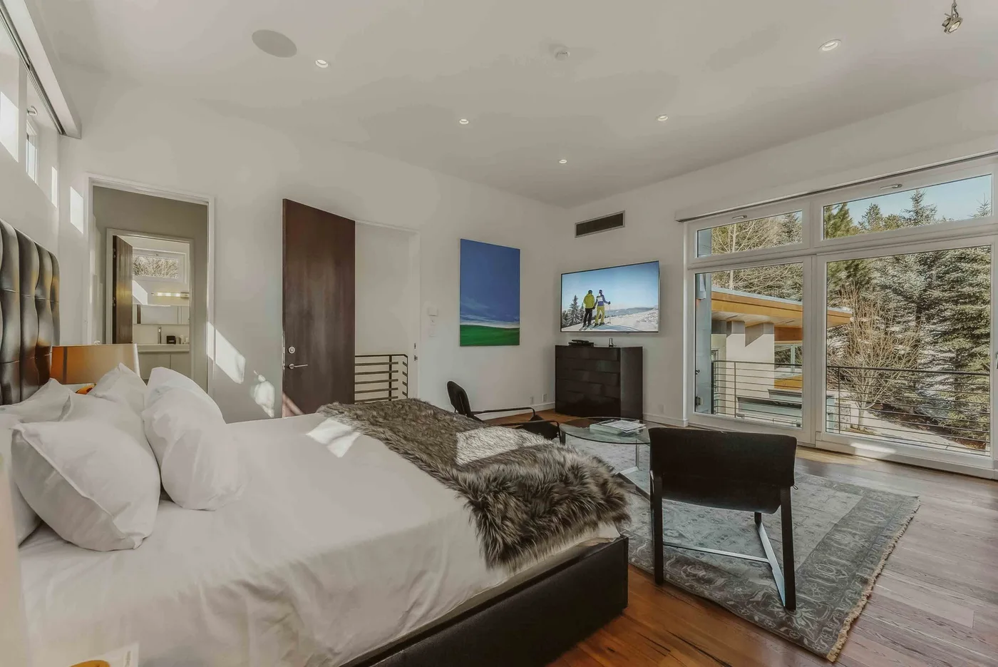 A bright bedroom with a large bed, seating area, and wide windows.