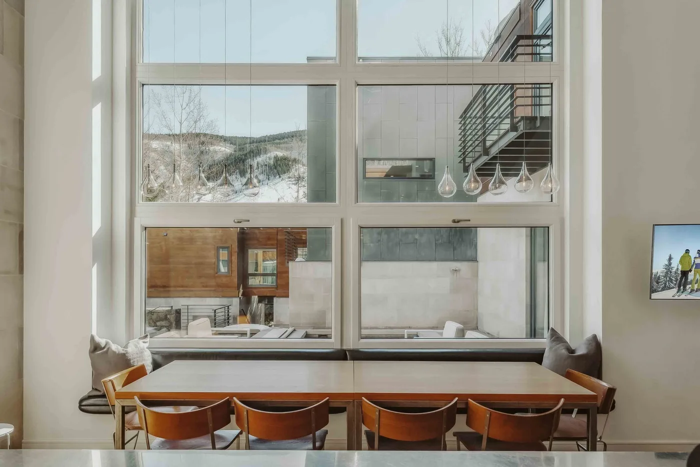 A dining table and chairs sit beside large windows overlooking nearby buildings.