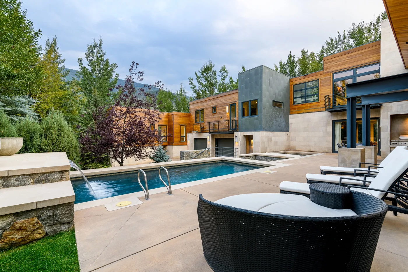 An outdoor pool beside a modern house, with lounge seating on the patio.