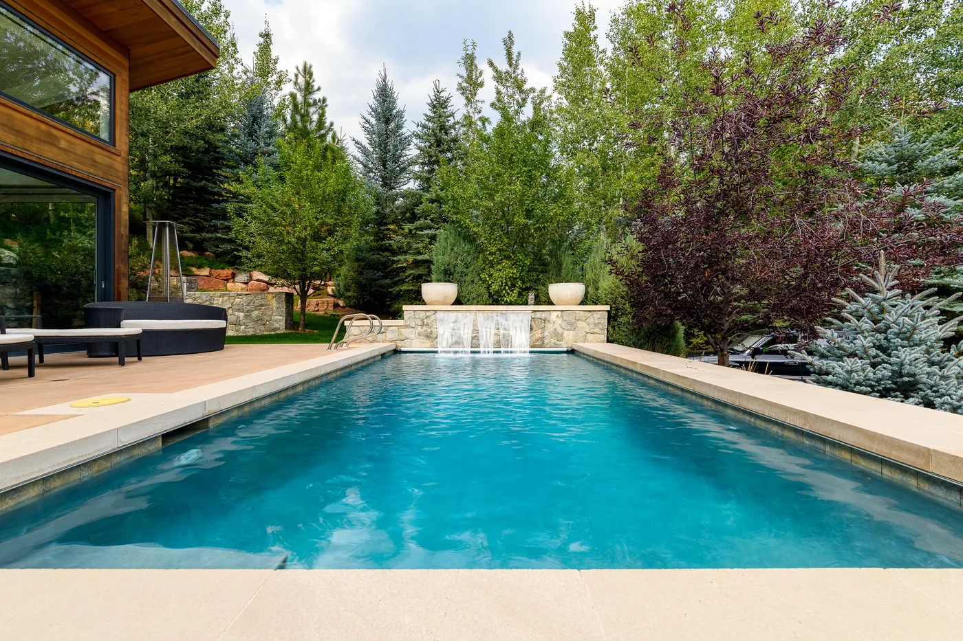 An outdoor swimming pool beside a modern house and surrounded by trees.