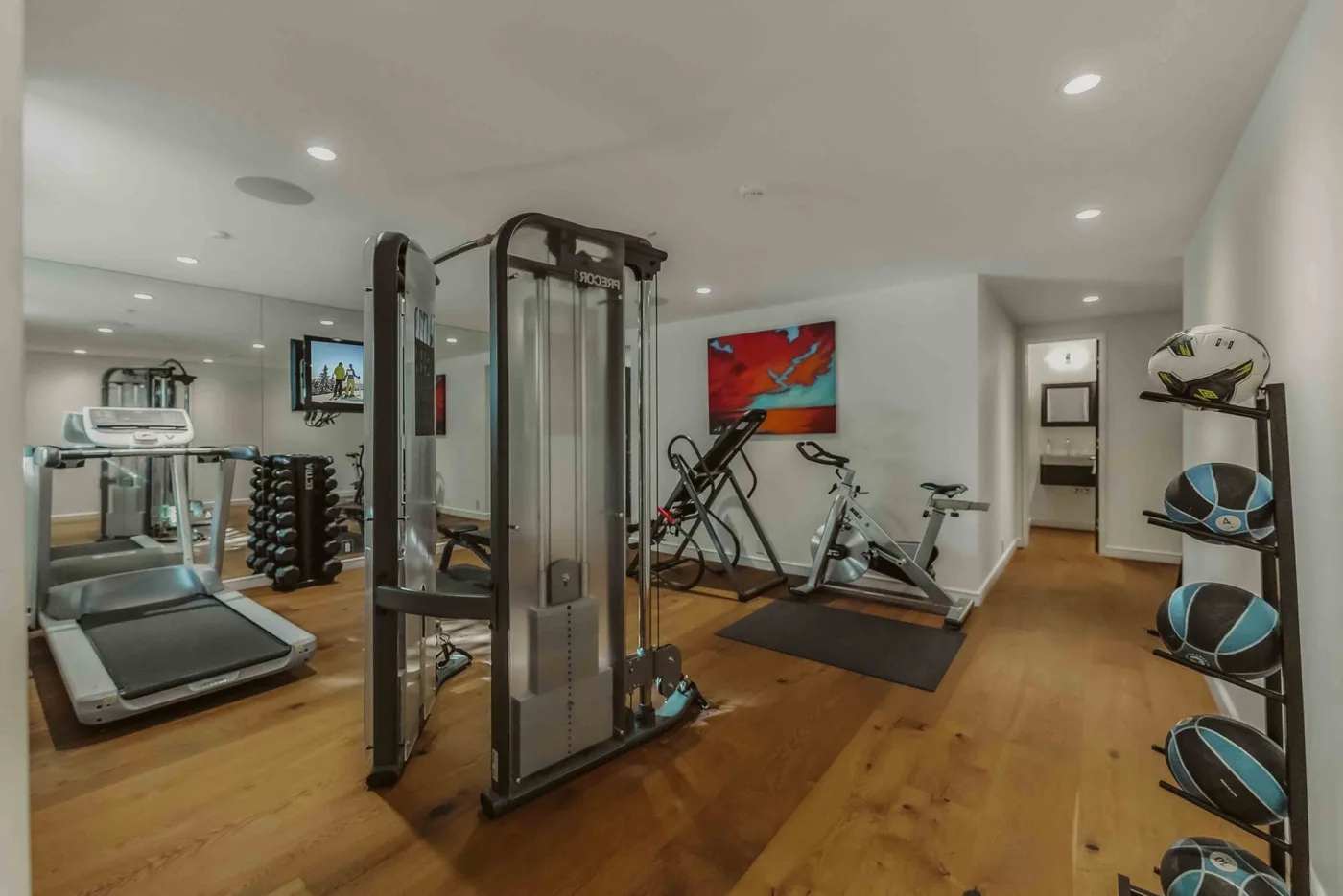 A home gym with exercise machines and weights on a wood floor.