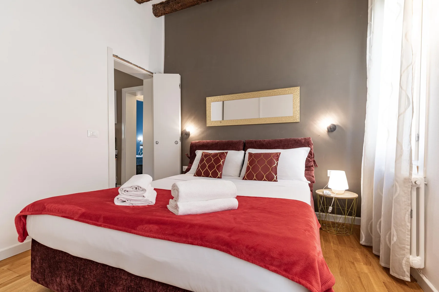 A bedroom with a bed dressed in red and white linens.