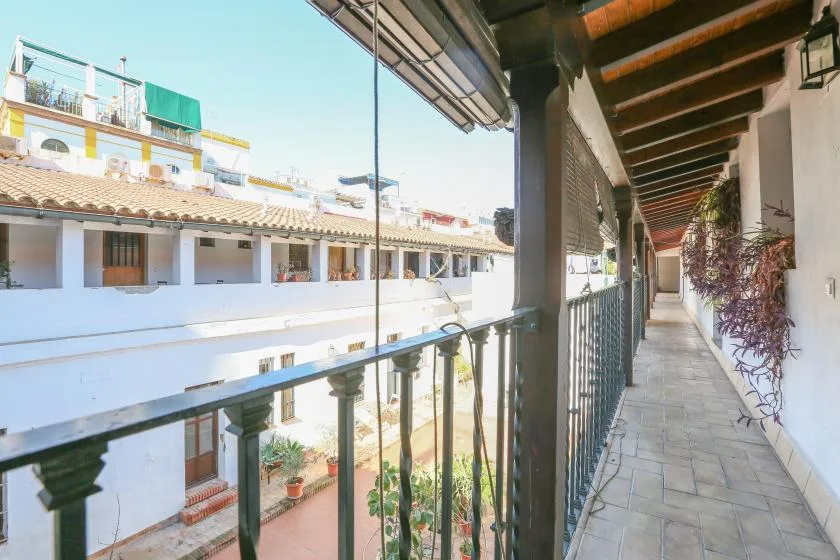 A covered outdoor corridor with a metal railing overlooks a bright courtyard.