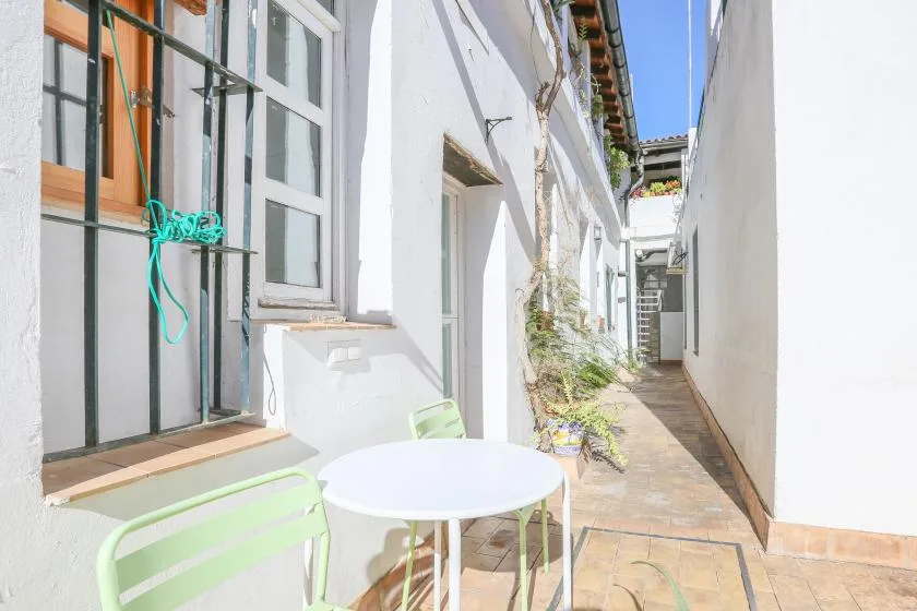 A narrow outdoor passage beside a white building has a small table and seating.
