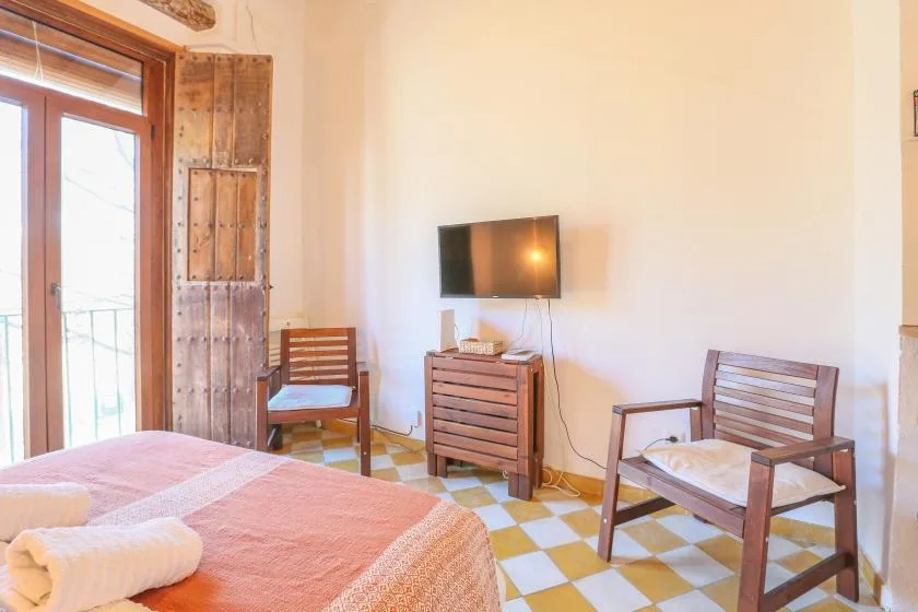 A bedroom with a bed, wooden seating, and a television mounted on the wall.