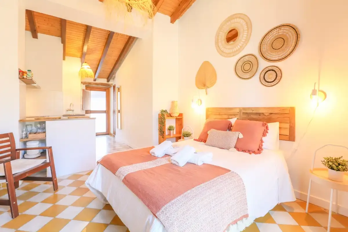 A bedroom with a bed, kitchenette, and exposed wooden ceiling beams.