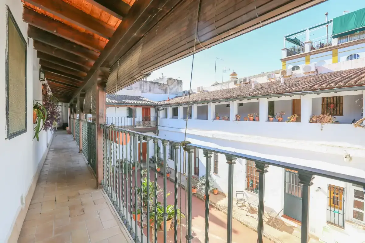 A covered balcony overlooks a courtyard with white buildings.