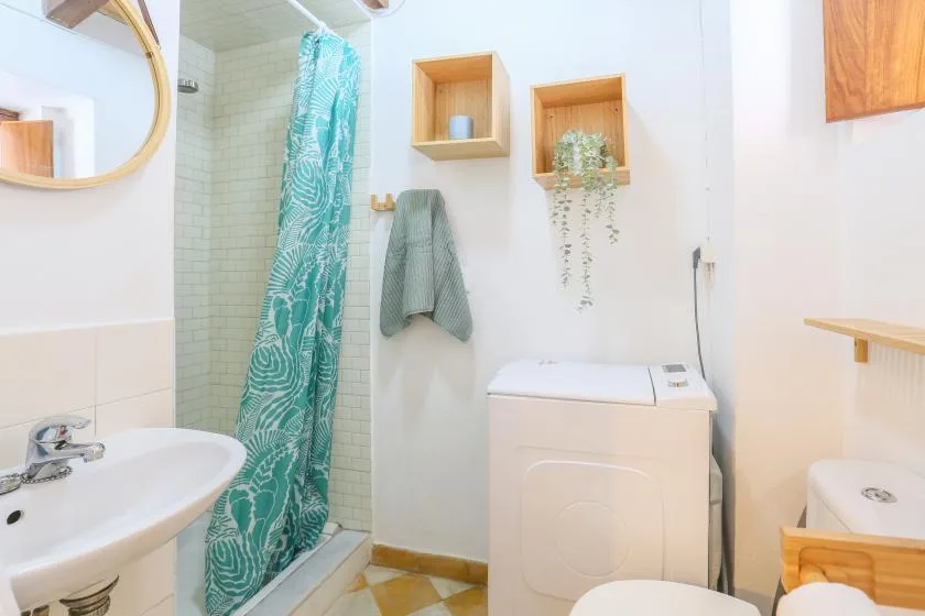 A bright bathroom with a sink, shower curtain, and washing machine.