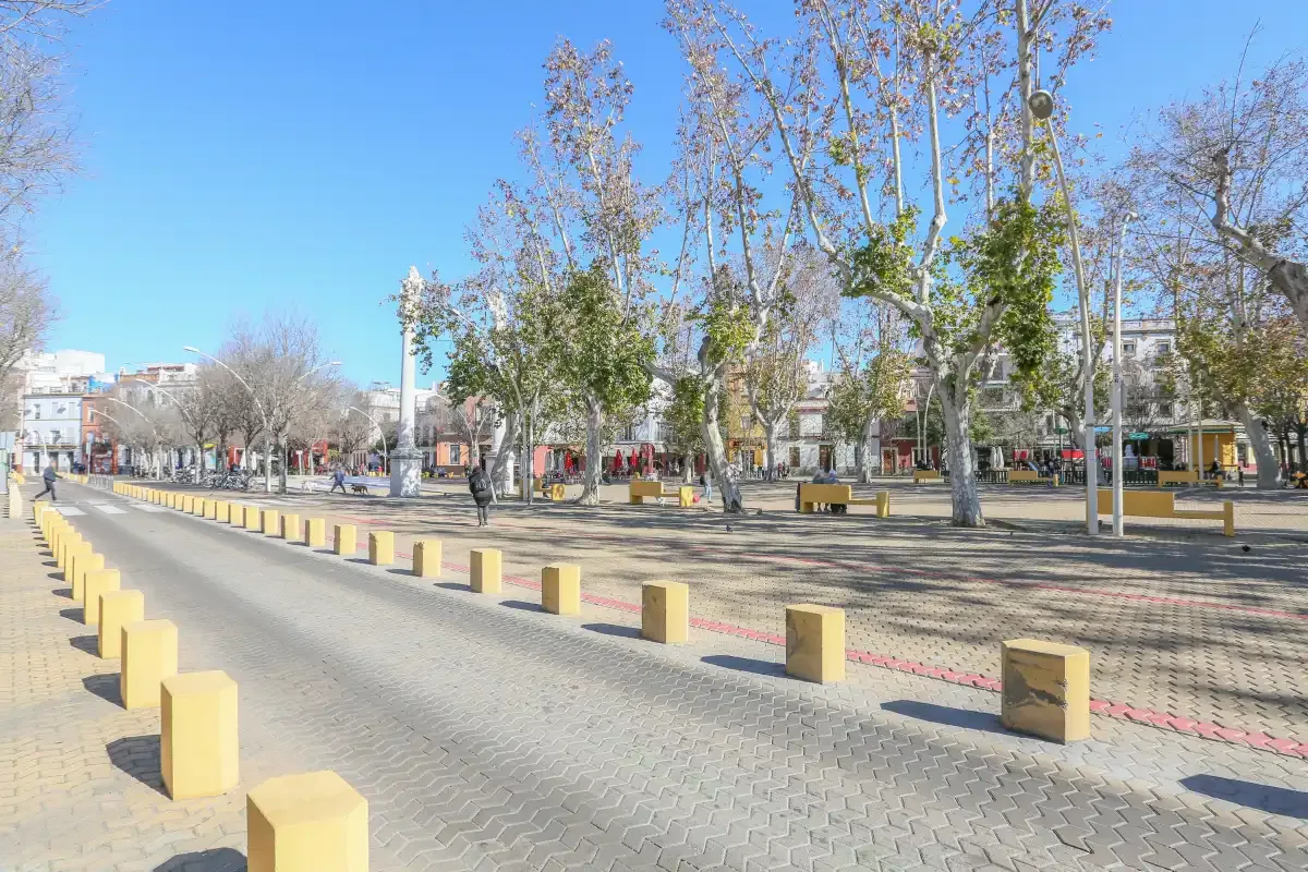 A broad paved plaza lined with trees and low yellow bollards.