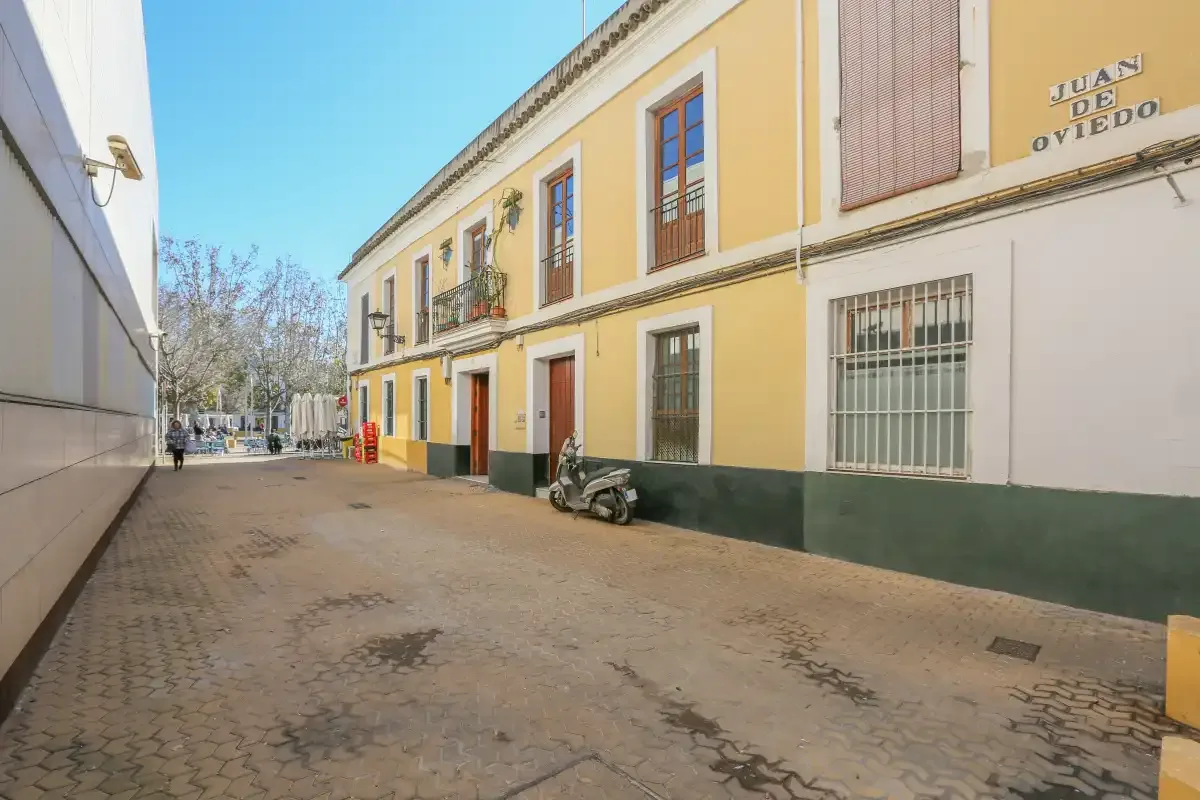 A paved street runs beside a yellow building with windows and balconies.