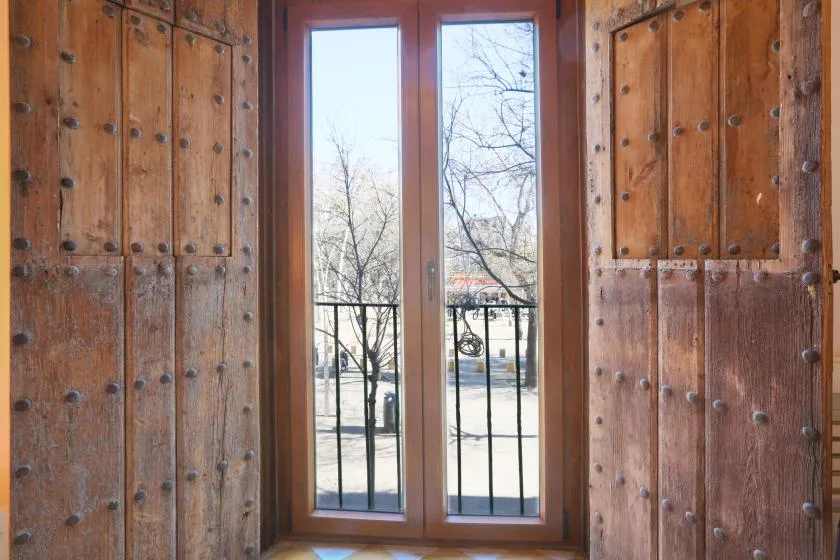 A tall window with dark metal railings overlooks a leafless winter landscape.