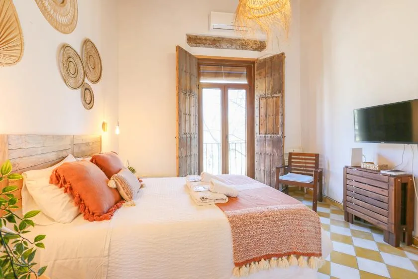 A bright bedroom with a neatly made bed and open wooden shutters.