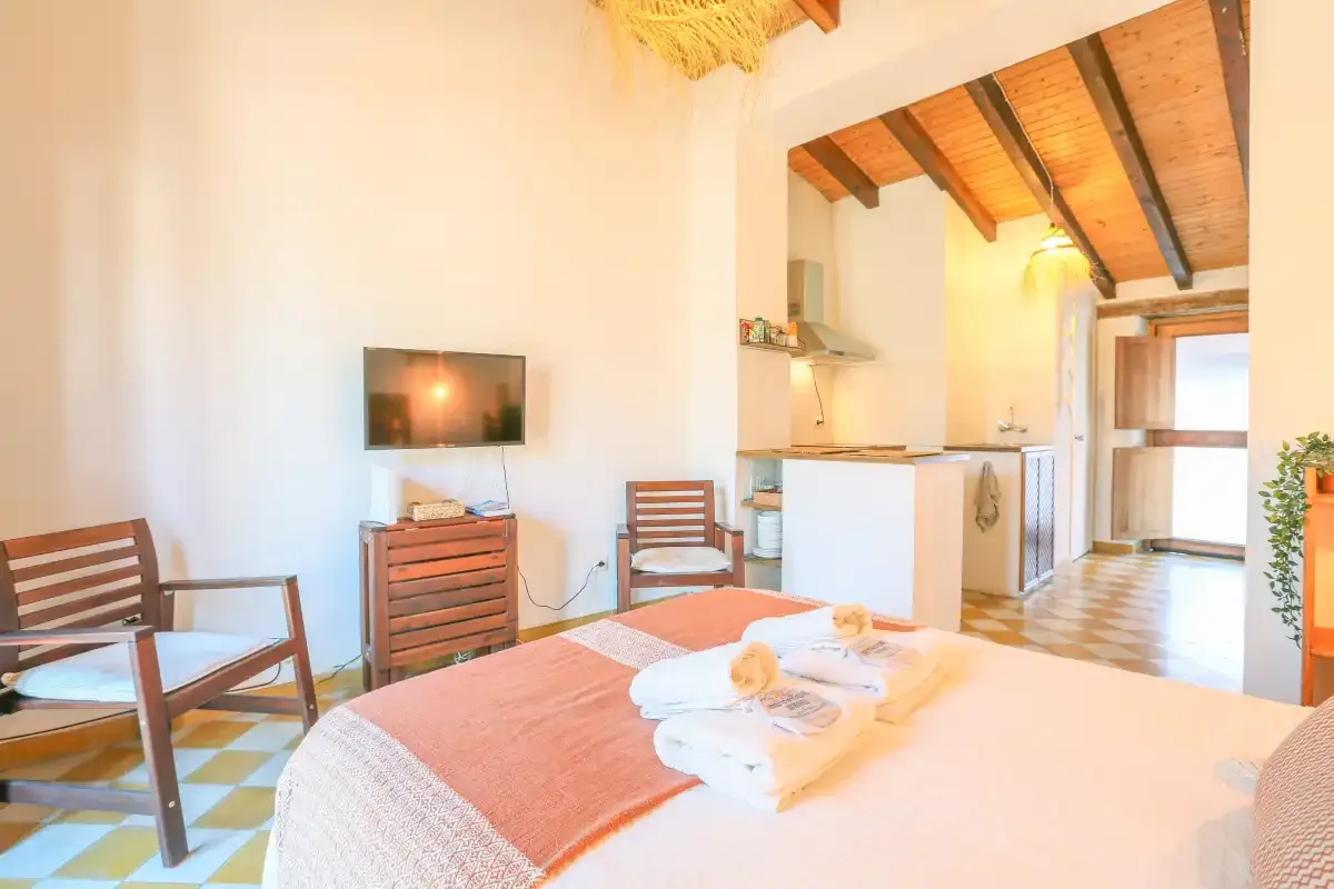 A bedroom opens onto a compact kitchen, with exposed wooden ceiling beams.