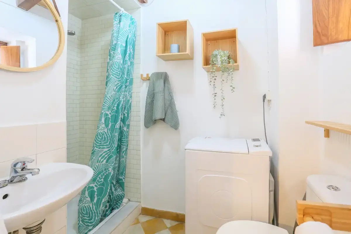 A bright bathroom with a sink, shower curtain, and washing machine.